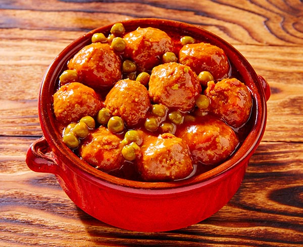 Albóndigas sin procesar en un tazón con los ingredientes en el fondo de madera